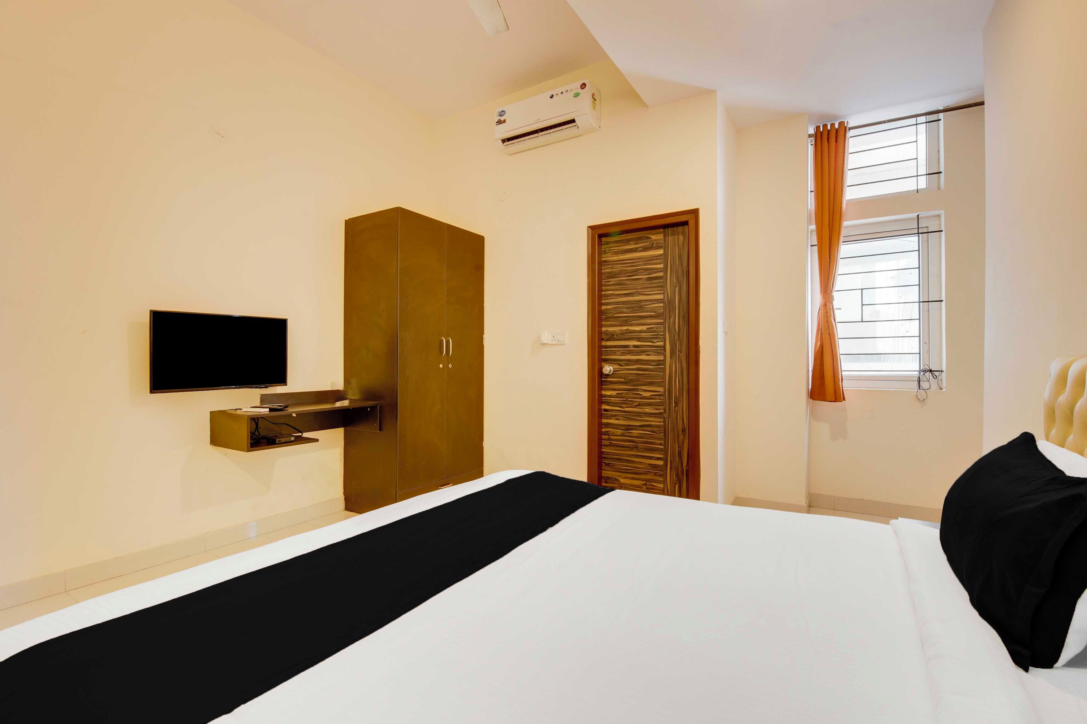 A hotel room with a bed, a TV, an air conditioning unit, a wardrobe, a door, and a window with curtains.