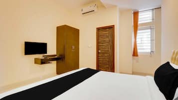 A hotel room with a bed, a TV, an air conditioning unit, a wardrobe, a door, and a window with curtains.