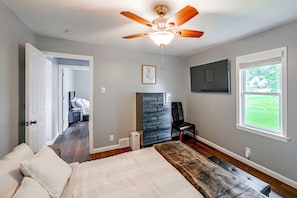 Une chambre à coucher comprenant un lit, un ventilateur de plafond, une commode, une chaise et une fenêtre donnant sur l’extérieur.