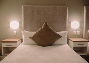 Una cama con cabecera capitonada, dos mesitas de noche y dos lámparas fijadas a la pared.