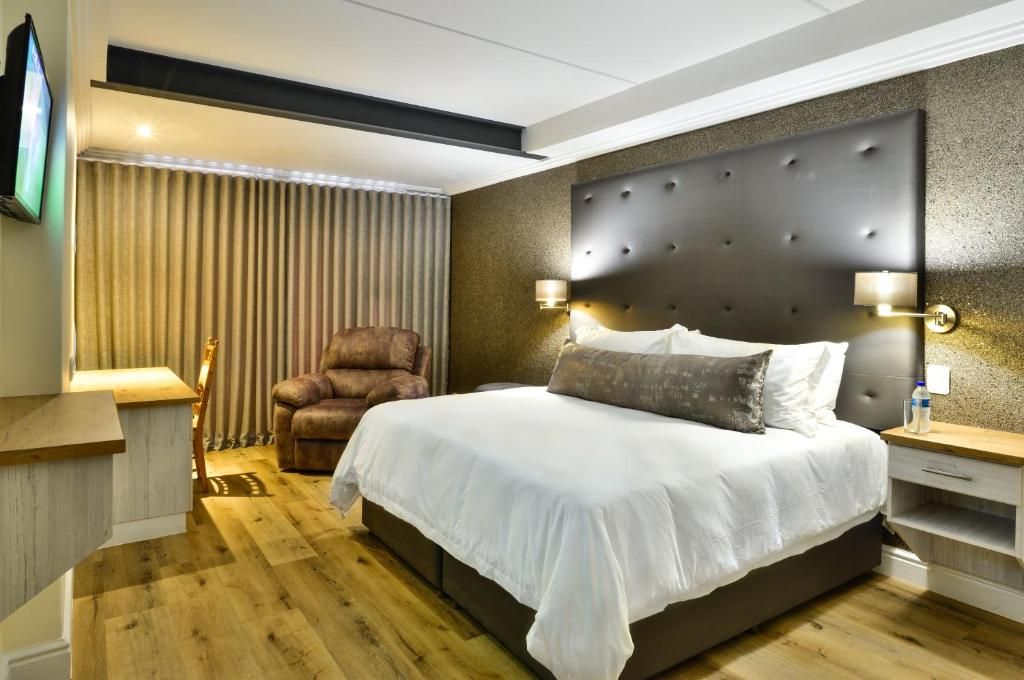 A modern hotel room with a large bed, a leather armchair, and a television mounted on the wall.