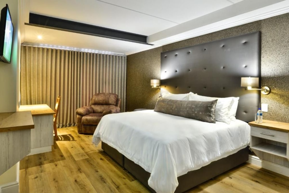 Een moderne hotelkamer met een groot bed, een leren fauteuil en een aan de muur bevestigde televisie.