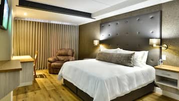 A modern hotel room with a large bed, a leather armchair, and a television mounted on the wall.