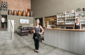 Een bar met een toonbank, planken vol flessen, en een trap naar een hoger niveau.