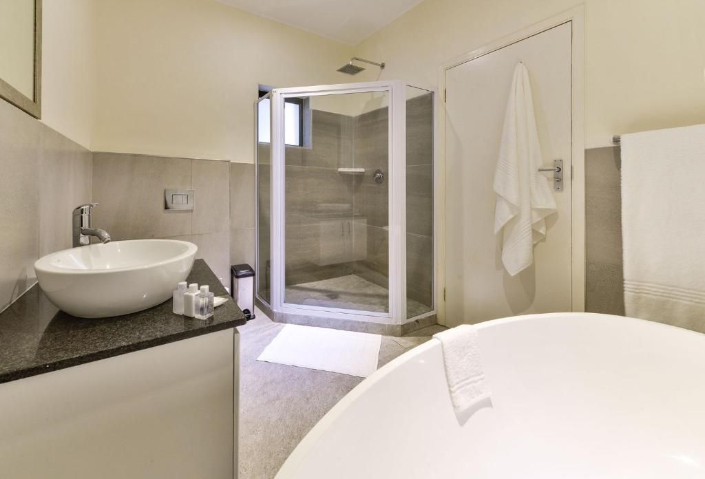 A bathroom with a large white bathtub, a round sink, and a glass-enclosed shower.