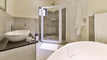 A bathroom with a large white bathtub, a round sink, and a glass-enclosed shower.