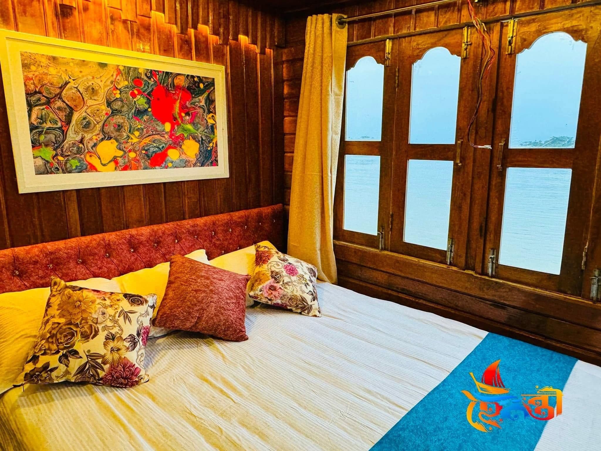 Une chambre d’hôtel avec un lit, un tableau, une fenêtre avec des rideaux et une vue sur l’eau.