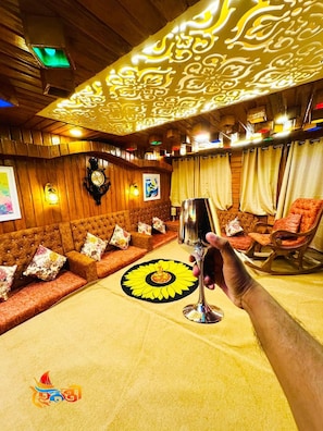 A room with a patterned ceiling, a sofa set, a table with a sun design, and a hand holding a glass.