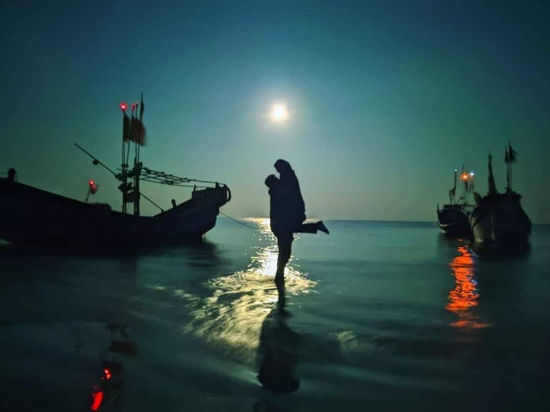 Una persona de pie sobre una superficie reflectante, con barcos al fondo.