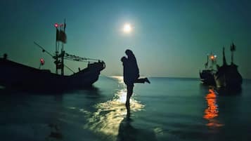 Una persona de pie sobre una superficie reflectante, con barcos al fondo.