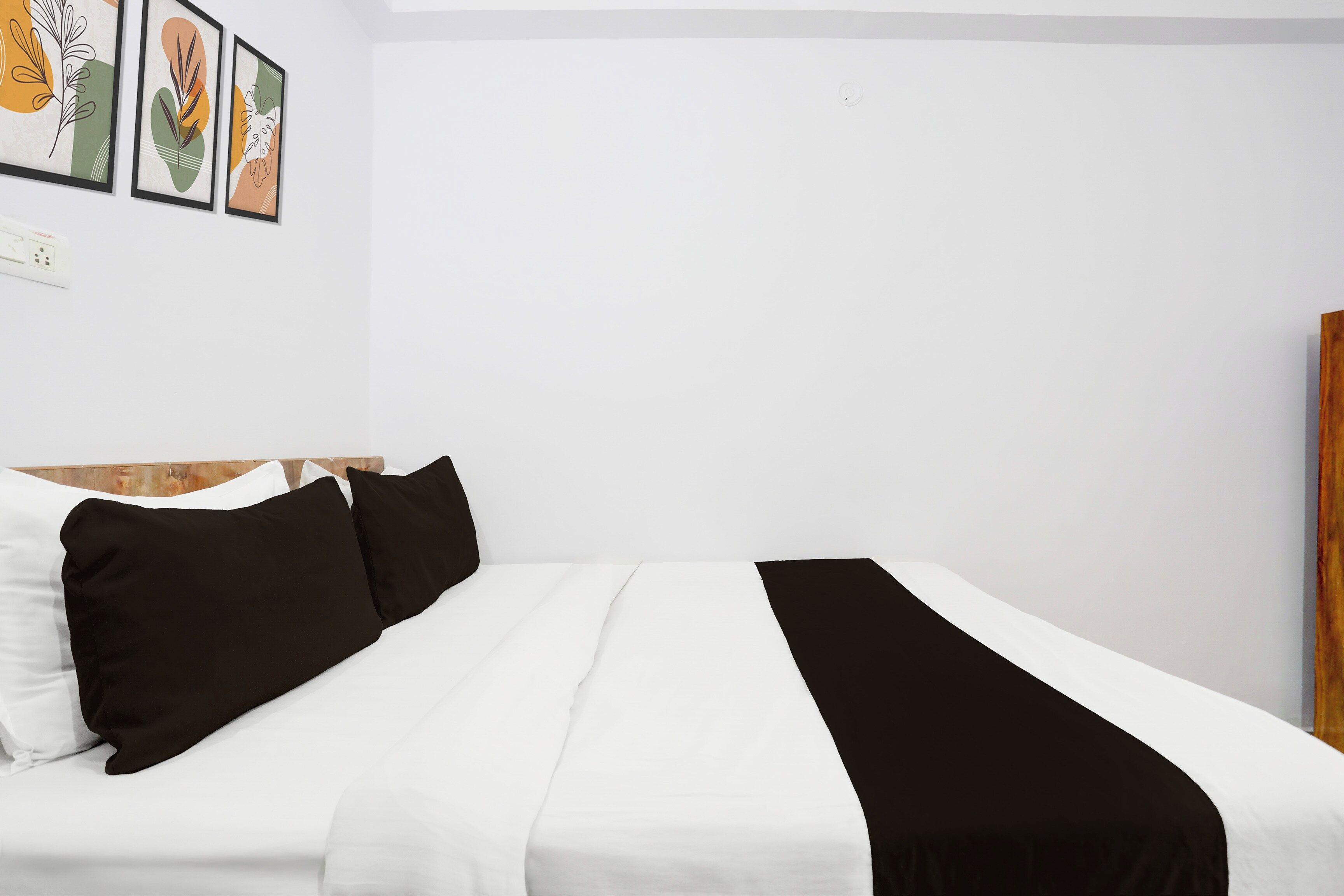 Una cama con ropa de cama blanca y negra, un cabecero de madera y una pared con obras de arte enmarcadas.