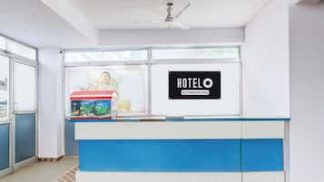 Mostrador de recepción de hotel con un cartel que dice 'HOTELO', una estatua y vistas al exterior.