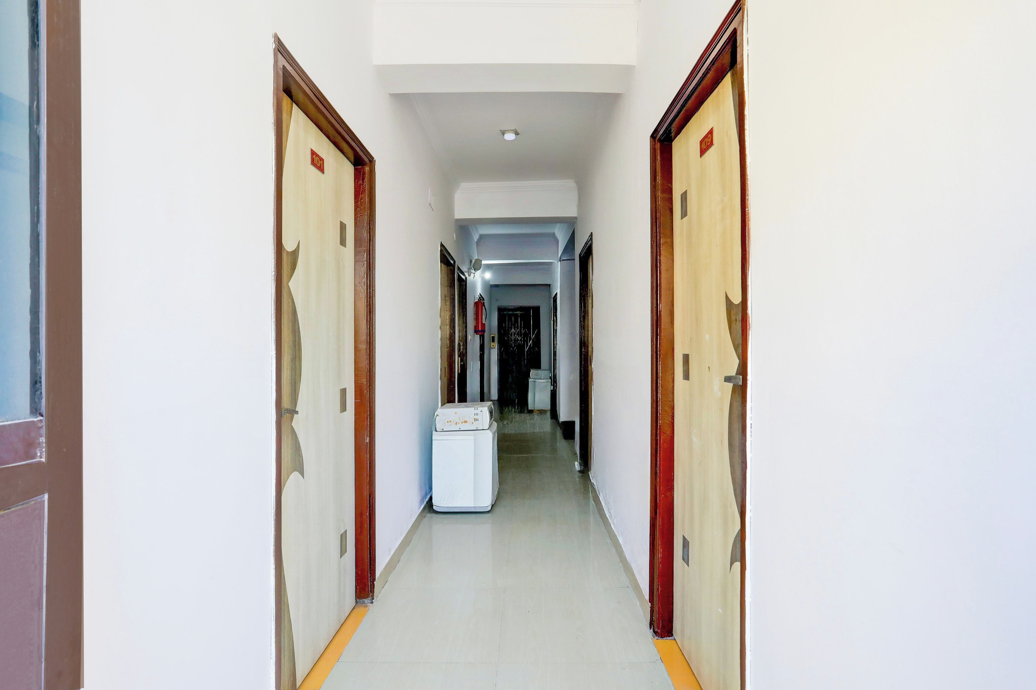 Um corredor com portas em ambos os lados, uma parede branca e uma luminária no teto.