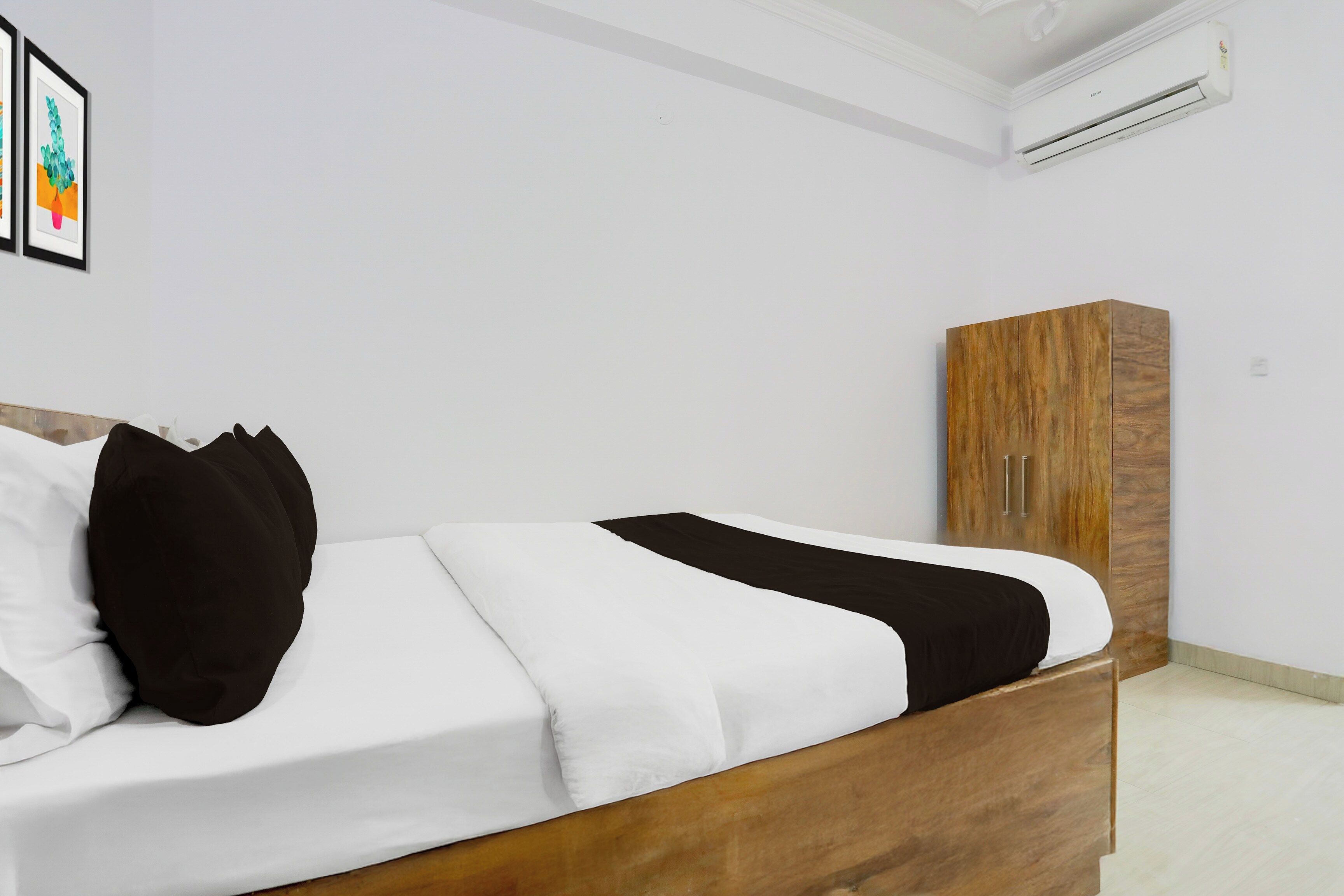 Cama bem arrumada com roupa de cama preta e branca, cabeceira de madeira e um guarda-roupa de madeira em frente a uma parede lisa.