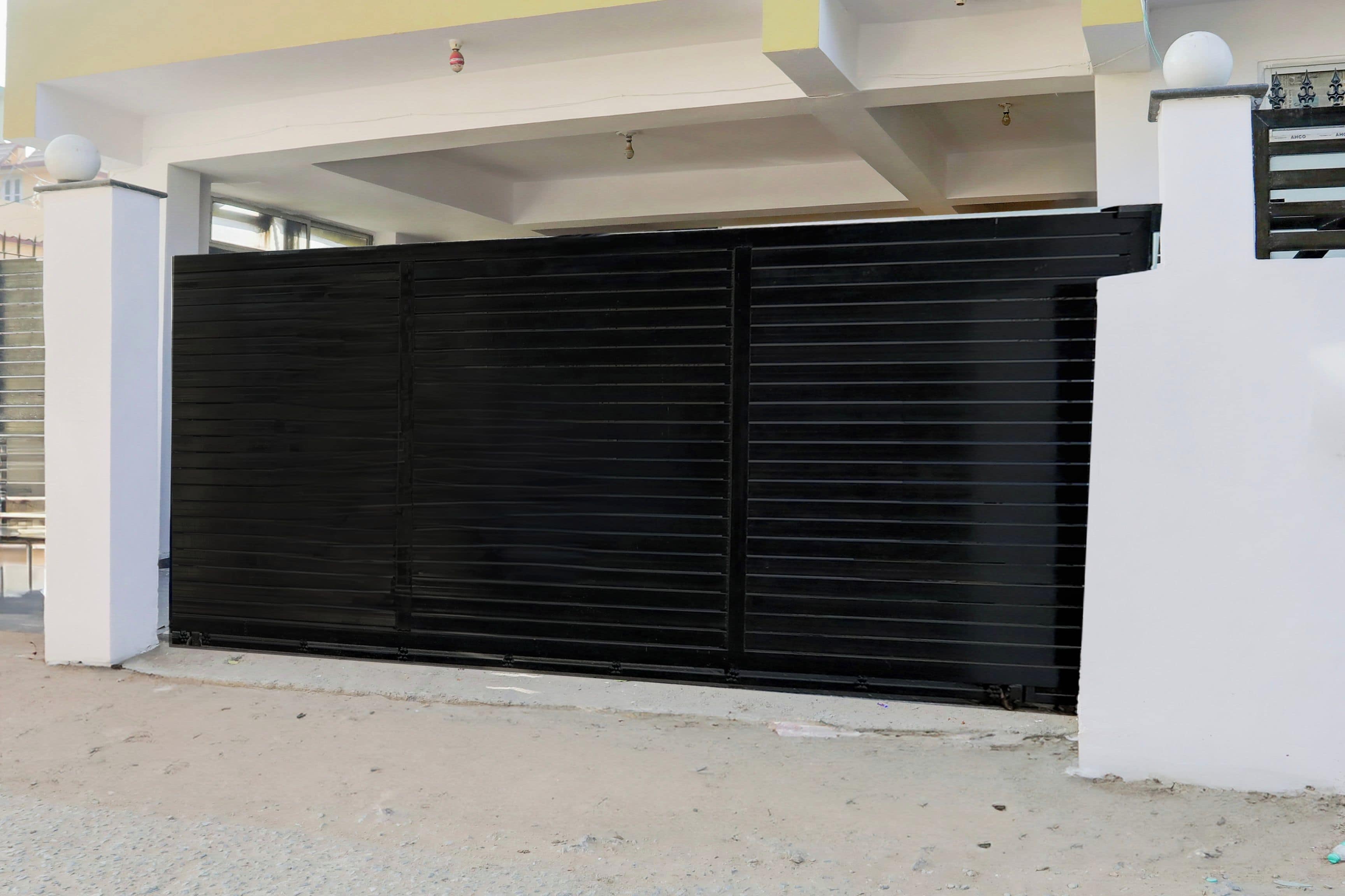 Una reja negra cerrada, un muro blanco y un suelo de concreto.