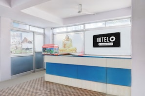 En hotelreception med en stor Buddha-statue, et indrammet plakatbillede af bybilledet, og et skilt der angiver, at hotellet serviceres af virksomheden.