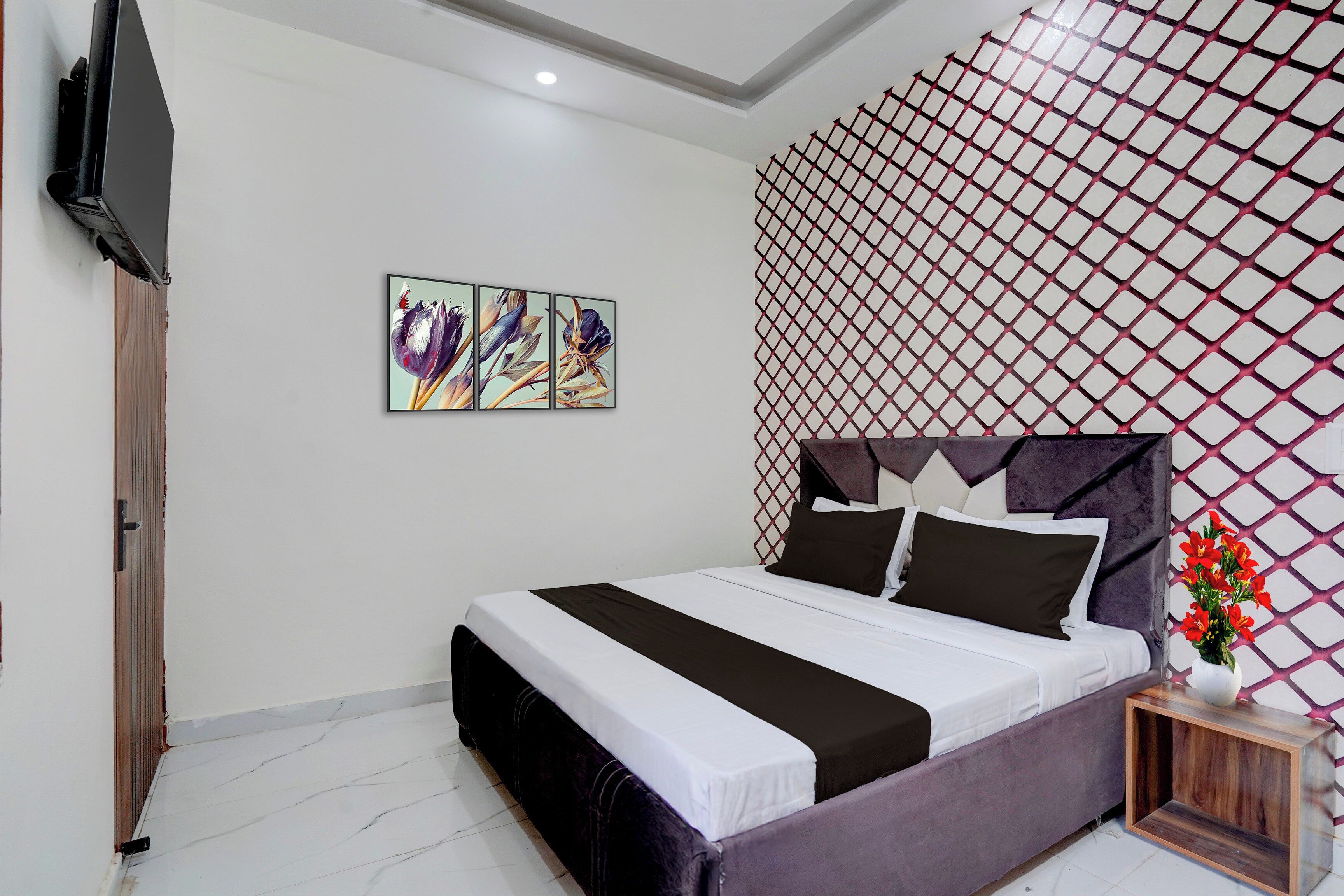 Un dormitorio con una cama, un televisor, una obra de arte en la pared y un papel tapiz estampado.
