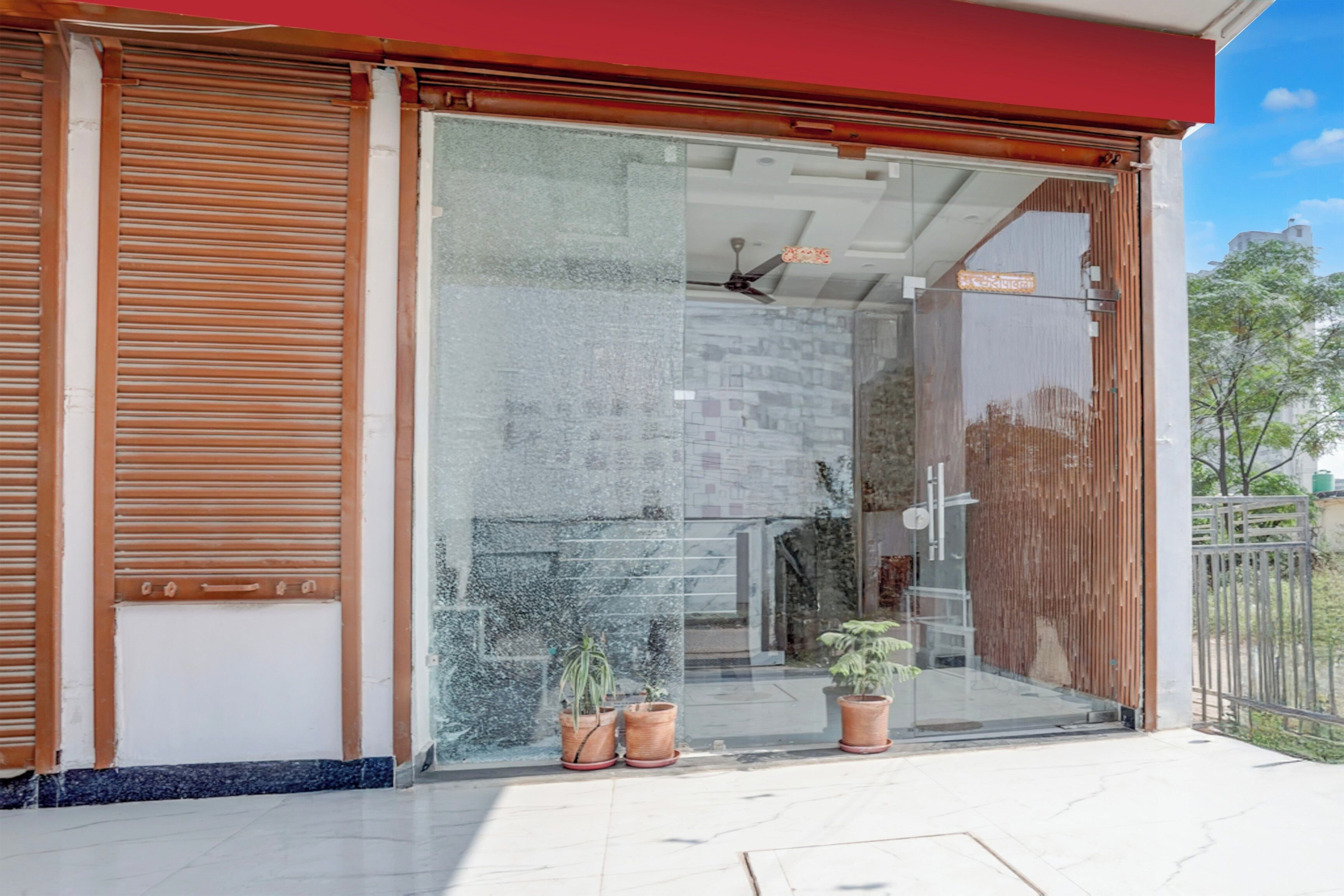 Un edificio moderno con entrada de vidrio, plantas en macetas y un ventilador de techo visible.