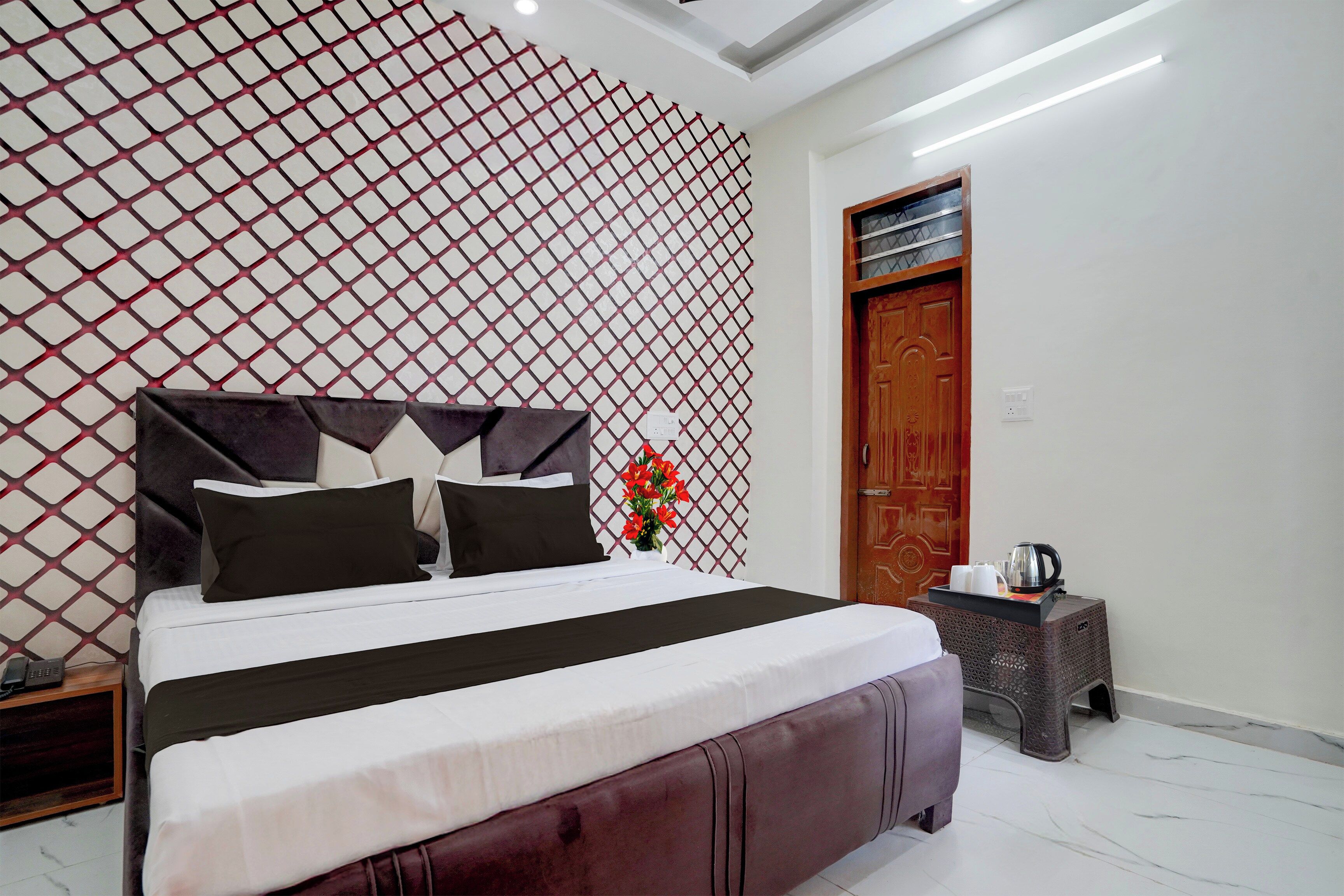Una habitación de hotel moderna con una cama grande, un muro decorativo, una puerta de madera y una pequeña mesita con un hervidor.