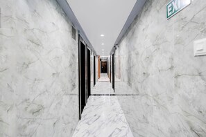 Un couloir au sol de marbre, avec des portes de chaque côté, un luminaire au plafond et un panneau indiquant la sortie de secours.
