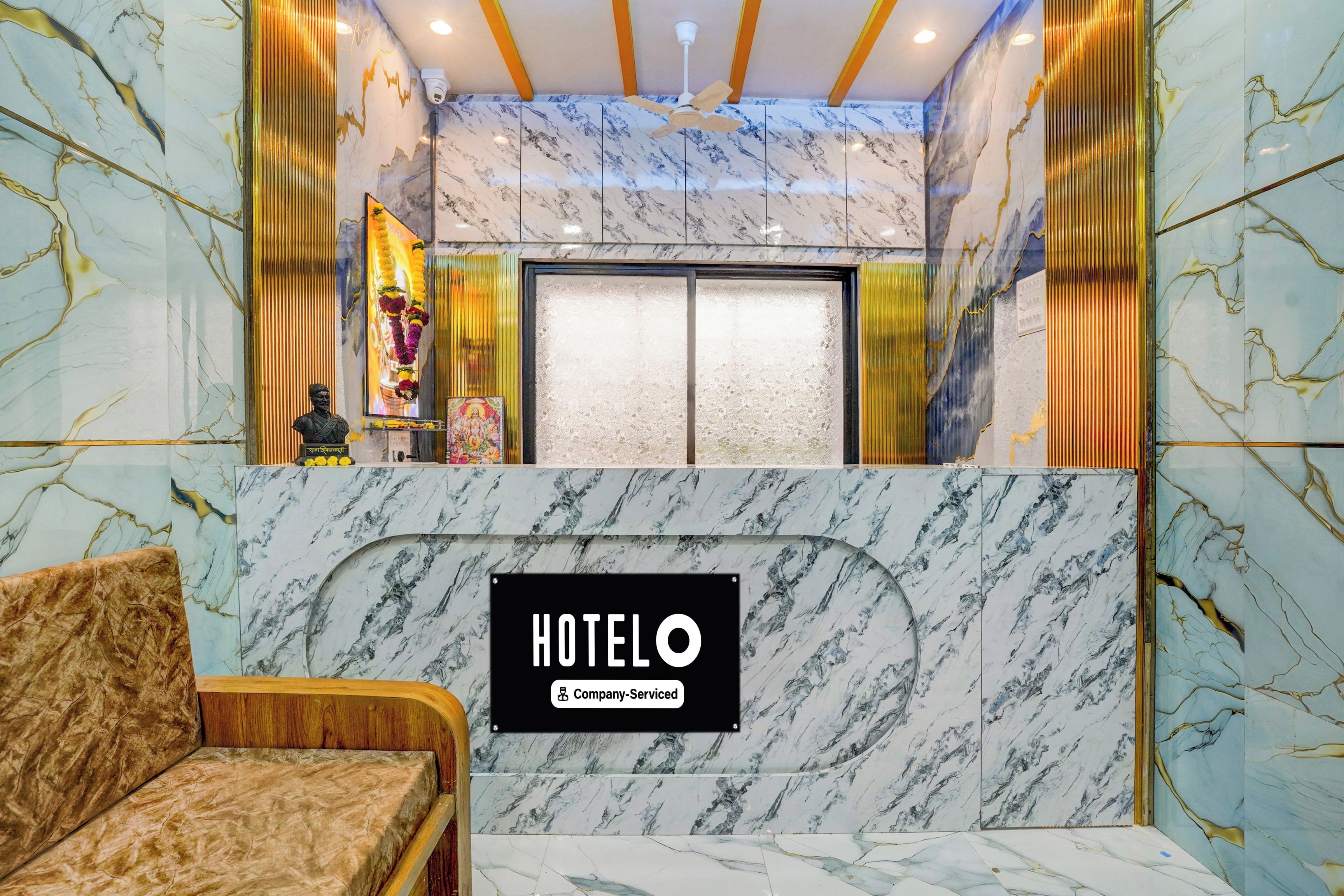 Zona de recepción de un hotel con un mostrador de mármol, un sofá y un ventilador de techo.