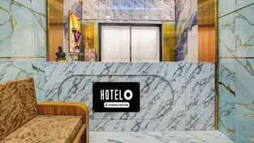Zona de recepción de un hotel con un mostrador de mármol, un sofá y un ventilador de techo.