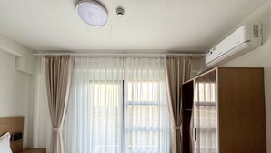 Hotellihuone, jossa on sänky, vaatekaappi, työpöytä ja ikkuna, jossa on verhot.