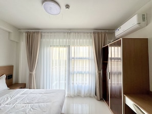 Quarto de hotel com cama, guarda-roupa, escrivaninha e janela com cortinas.