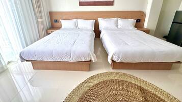 Habitación de hotel con dos camas, un ventanal con cortinas, un cuadro colgado en la pared y una alfombra tejida en el suelo.