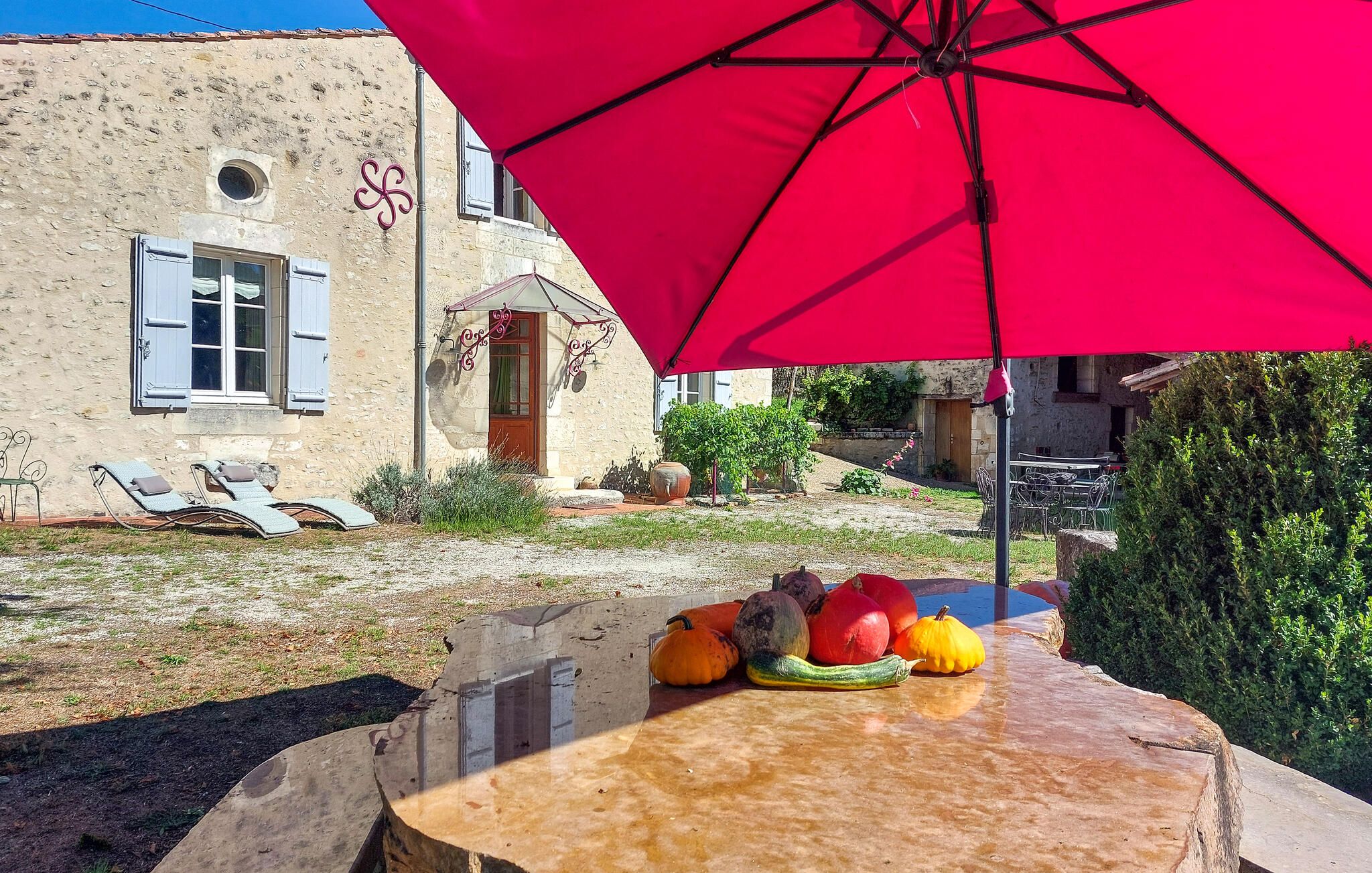 A stone building with a red umbrella, outdoor seating, and a table with pumpkins.