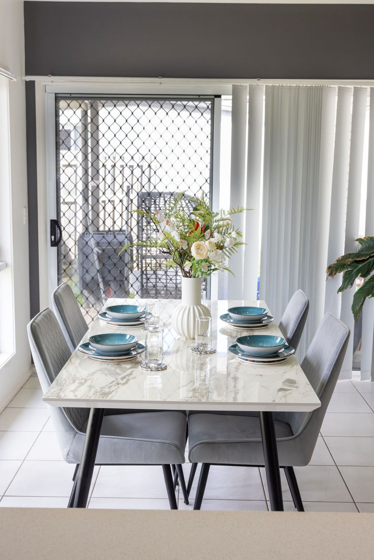 Un coin repas avec une table en marbre, des chaises grises et un vase rempli de fleurs.