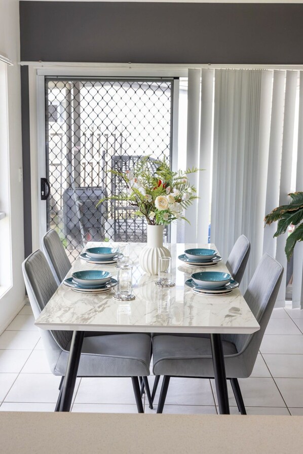A dining area with a marble table, grey chairs, and a vase with flowers.