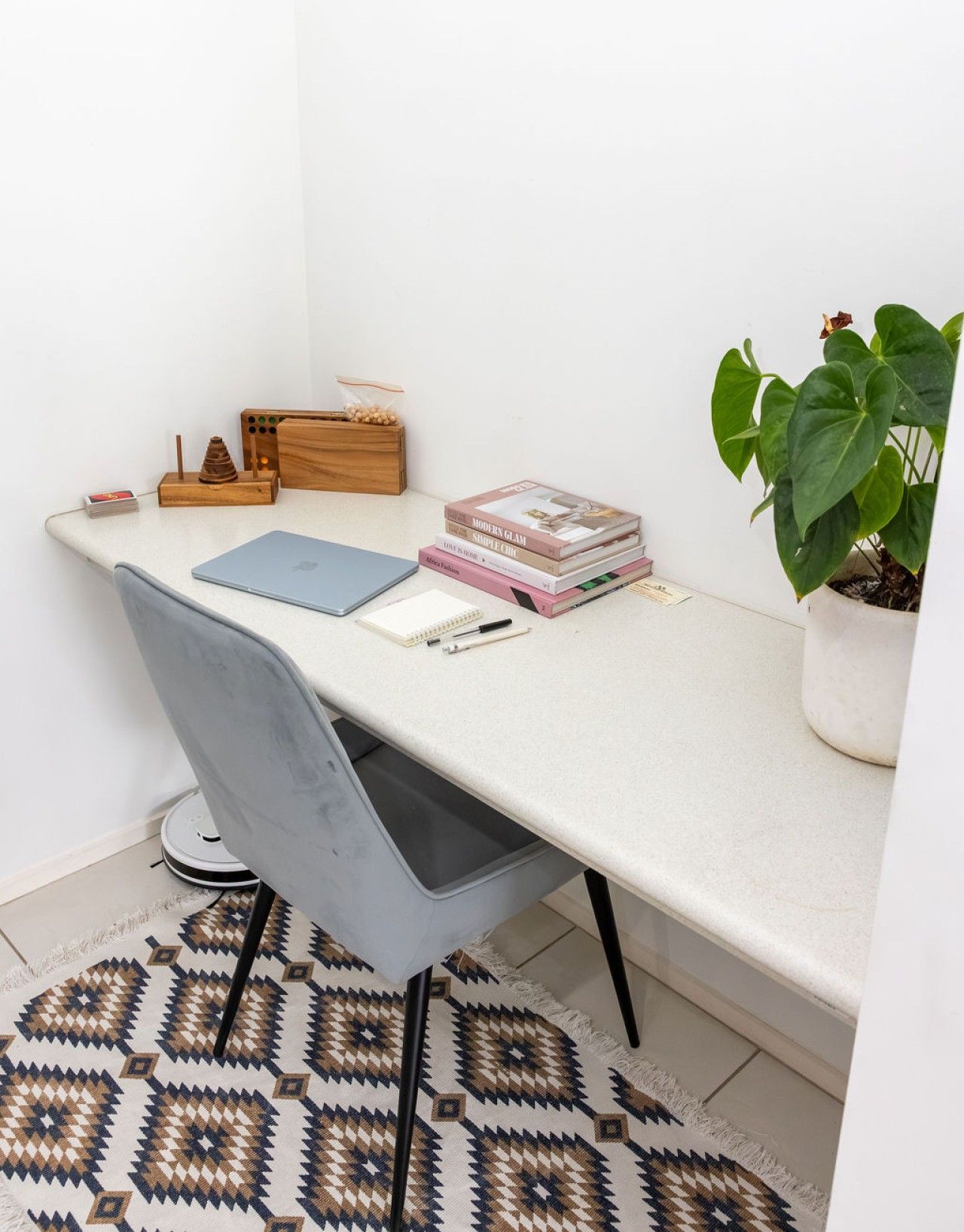Espacio de trabajo en esquina con escritorio, silla, libros, planta y una caja de madera pequeña.