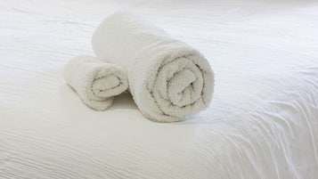 Un lit bien fait, avec du linge de lit blanc et deux serviettes blanches roulées.
