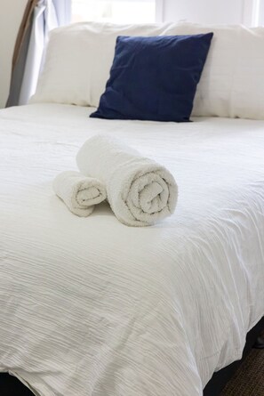 A neatly made bed with white bedding and two rolled white towels.