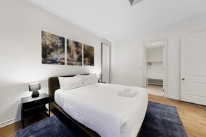 A modern hotel room with a large bed, a nightstand, a lamp, and a painting on the wall. - Spacious 3-bed Apartment in Melbourne CBD (Melbourne)