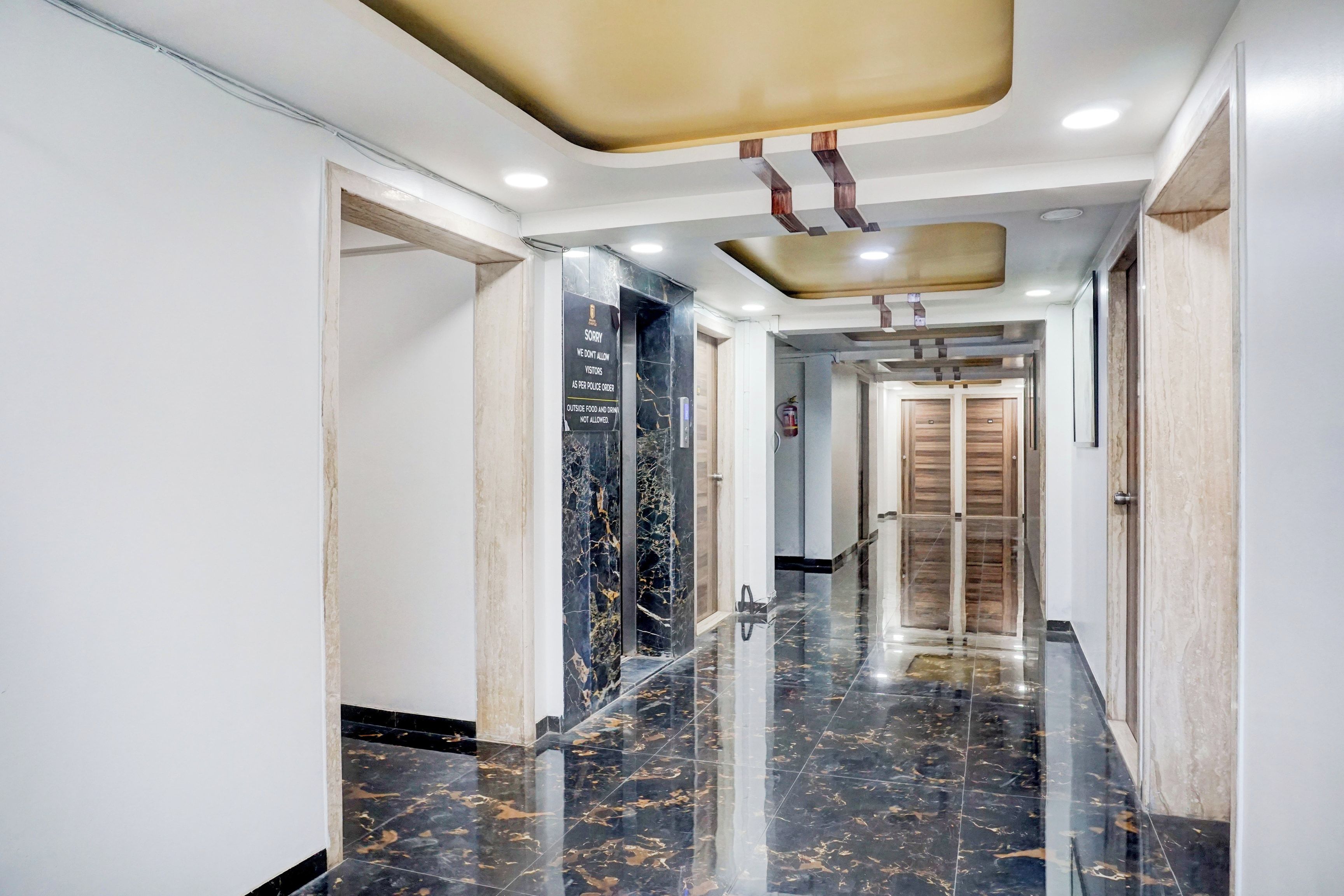 Corredor com piso de mármore, teto com iluminação embutida e porta de madeira no final.