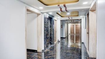 Corredor com piso de mármore, teto com iluminação embutida e porta de madeira no final.