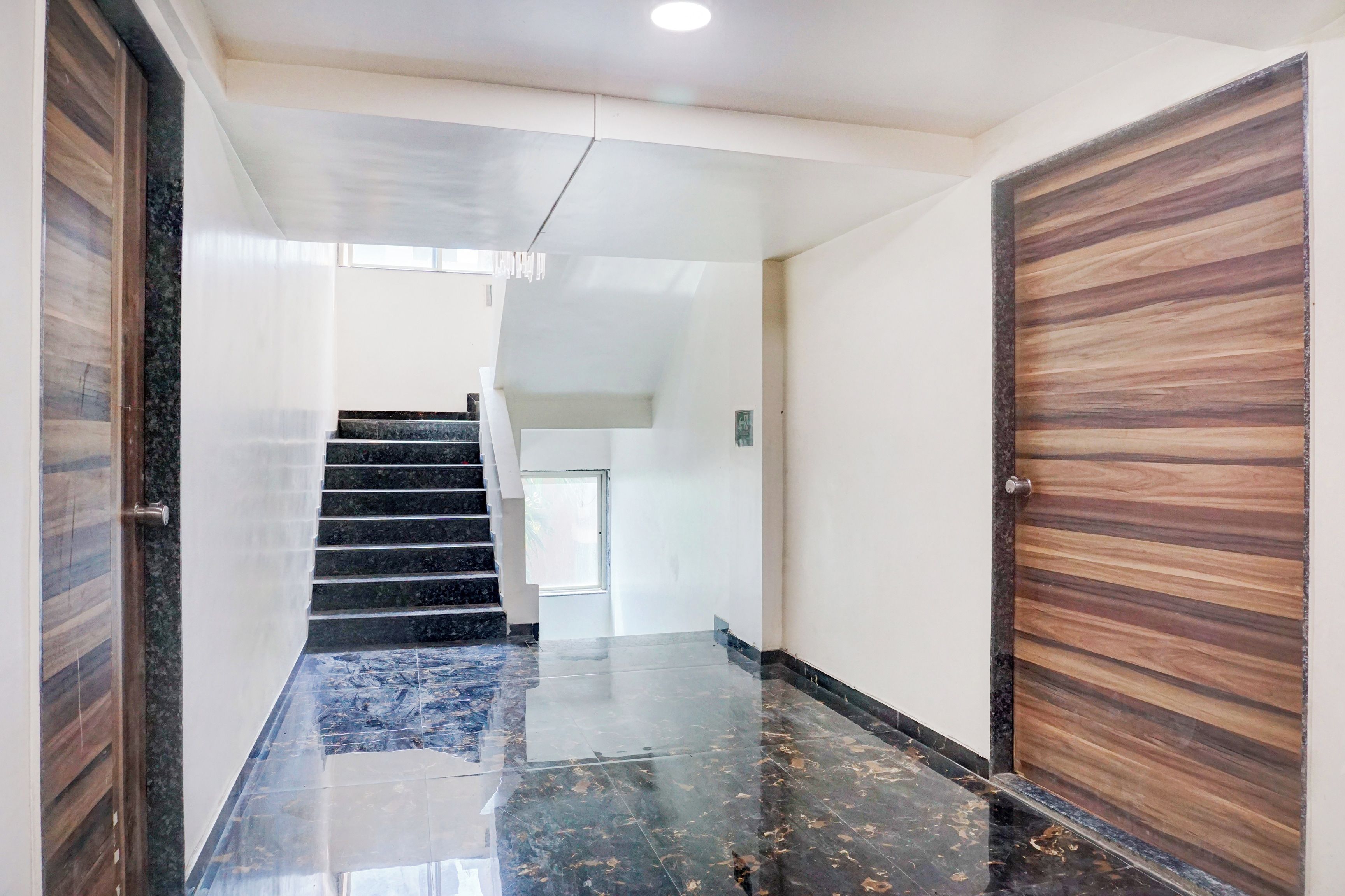 A hallway with a marble floor, a staircase, and wooden doors.