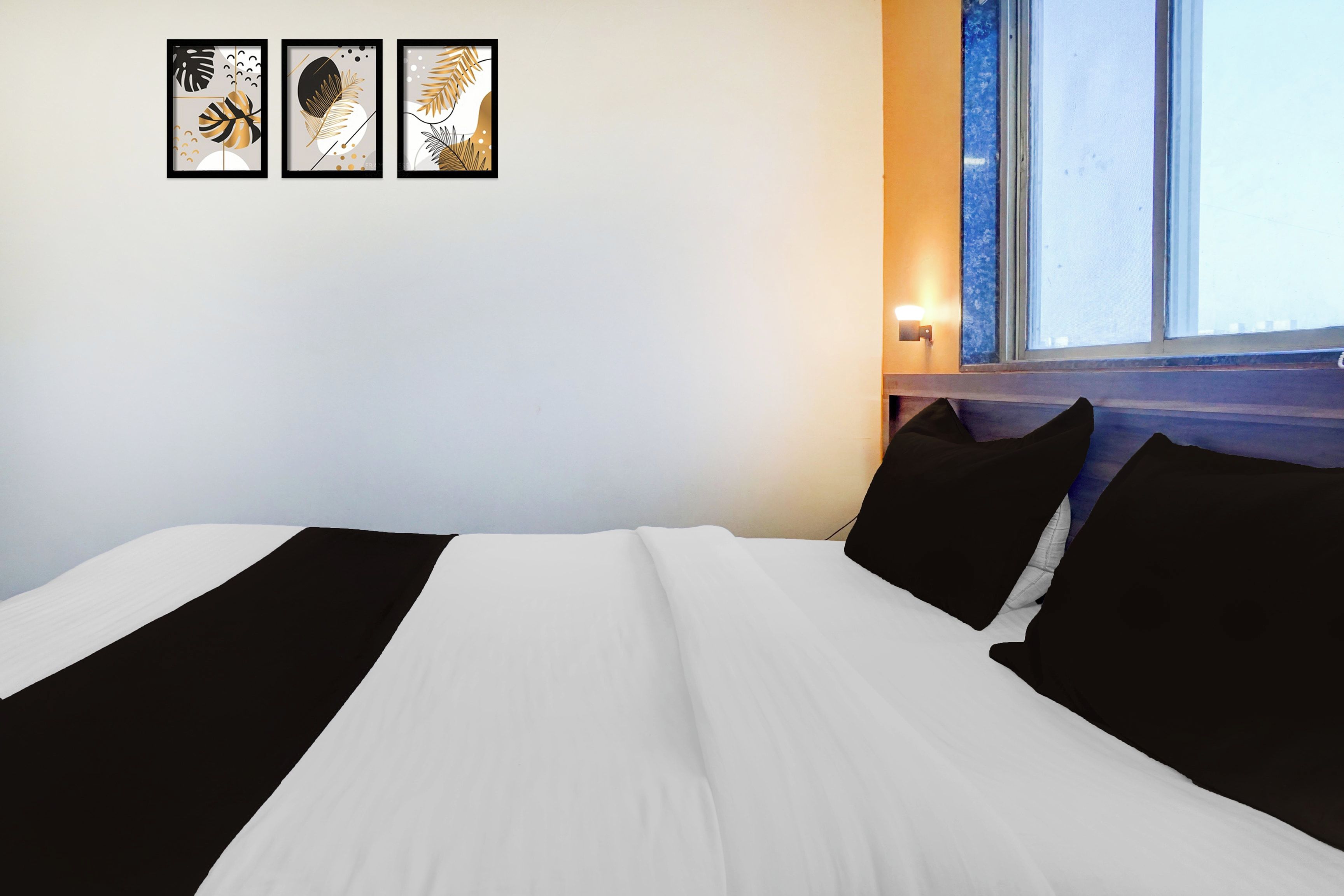 A hotel room with a bed, a window, and three framed artworks on the wall.