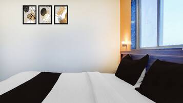 A hotel room with a bed, a window, and three framed artworks on the wall.