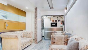 A modern living room with a sofa set, a glass partition, and a reception desk with a clock and fire extinguisher. - Townhouse Oak Shivsrushti Historical (Pune)