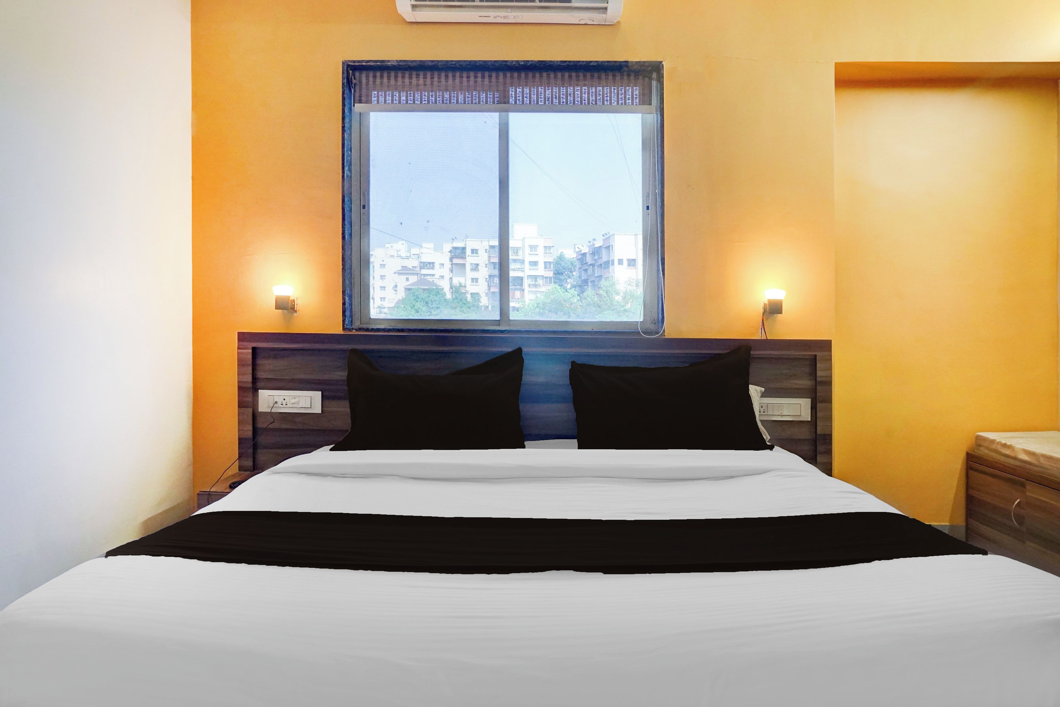 A hotel room with a bed, a window, and two wall-mounted light fixtures.