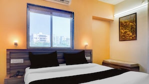 A hotel room with a bed, a nightstand, a bedside table, a window with a view of buildings, and a wall-mounted light fixture. - Townhouse Oak Shivsrushti Historical (Pune)