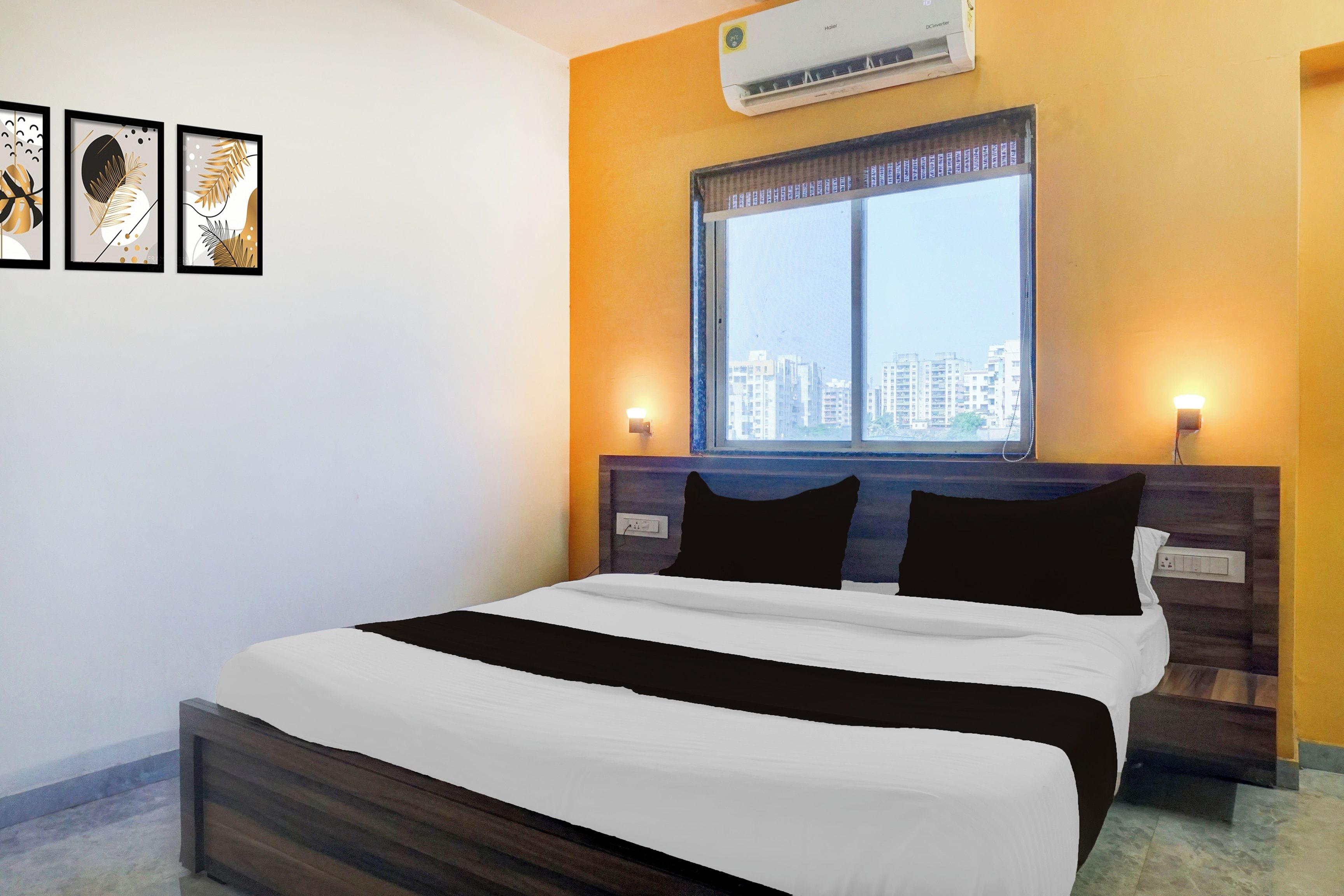 Habitación de hotel con cama, ventana con vista a la ciudad, aire acondicionado y decoración en la pared.