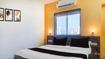 Habitación de hotel con cama, ventana con vista a la ciudad, aire acondicionado y decoración en la pared.