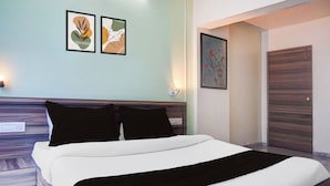 A hotel room with a bed, two wall-mounted light fixtures, and two framed artworks above the bed. - Townhouse Oak Shivsrushti Historical (Pune)