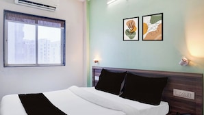 A hotel room with a bed, a window with a view of buildings, two wall-mounted light fixtures, and a wall socket. - Townhouse Oak Shivsrushti Historical (Pune)