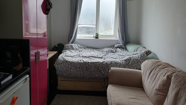 Una camera compatta con un letto, una piccola scrivania, un angolo cottura e una finestra con tende.