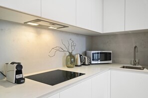 A modern kitchen with white cabinetry, a black induction cooktop, a microwave, a kettle, and a coffee maker. - Elevated 1-bed Apartment Near Melbourne CBD (Melbourne)
